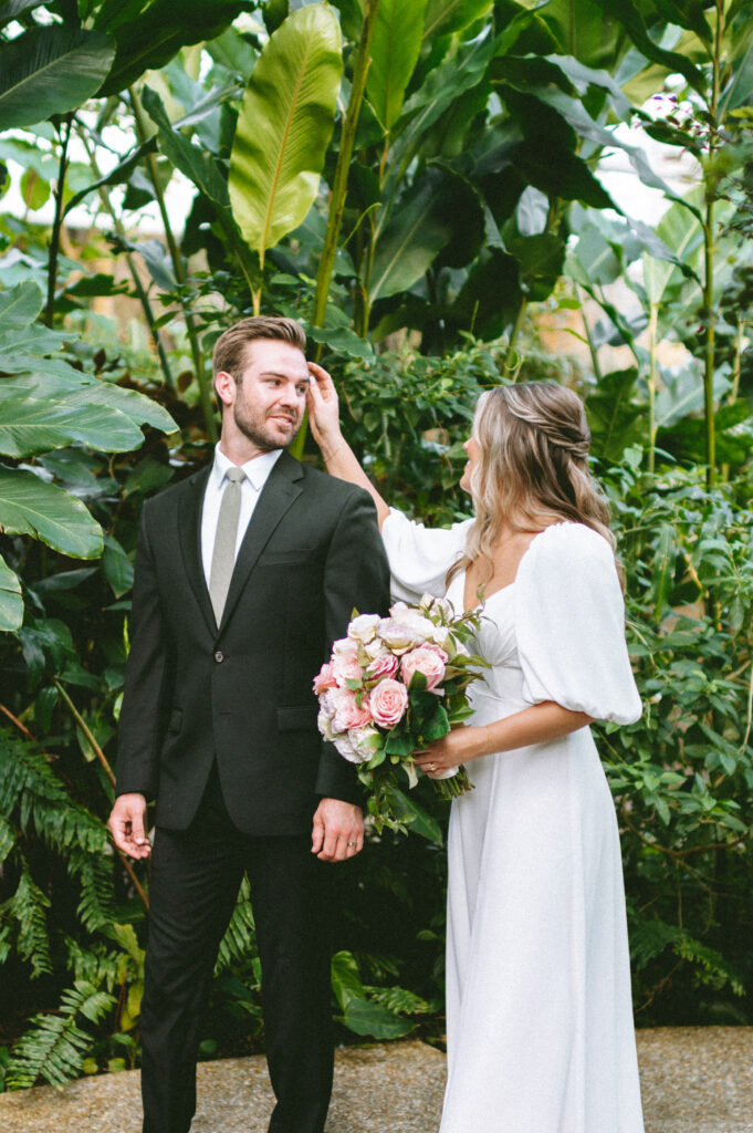 Bride touching groom's hair surrounded by greenery
