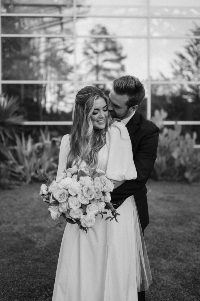 Black and white image of groom hugging bride from behind.